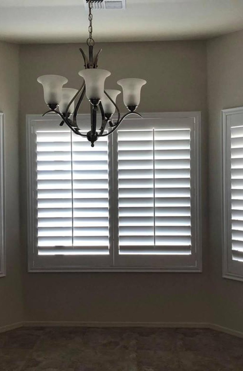 white plantation shutters across a three-window bay in a dining room
